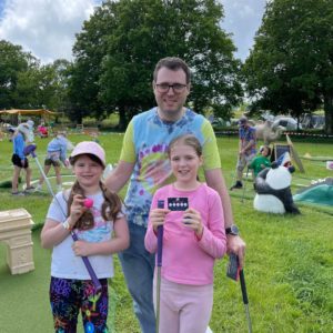 Man and his two daughters standing with mini golf putters