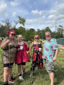 Three women and one man standing together with mini golf clubs at a music festival